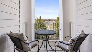 Een balkon met twee stoelen en een tafel, met uitzicht op bomen en een heldere lucht.