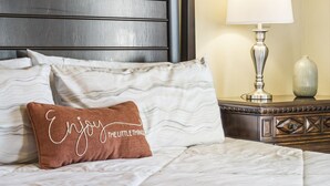 Een netjes opgemaakt bed met een kussen waarop staat: 'Geniet van de kleine dingen'.
