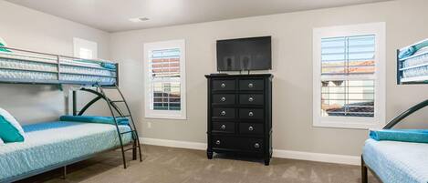A room with bunk beds, a black dresser, and a television on the wall.
