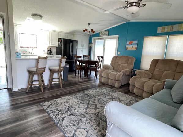 A spacious living room with a patterned rug, a blue accent wall, and a dining area with wooden chairs and a table.