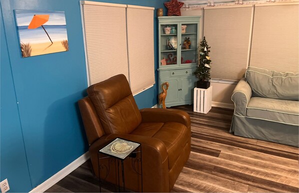 Et værelse med en læderlænestol i brunt, et lyseblåt skab, et lille juletræ og en beige sofa.