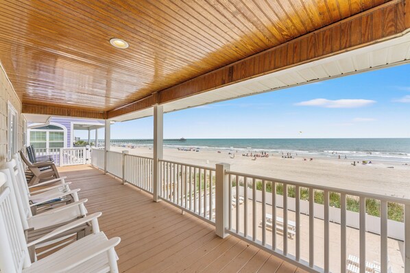 A covered outdoor area with a wooden deck, white railings, and a view of the beach and ocean. - Sea Aire II Duplex Up, Pet Friendly, Oceanfront, Shared Game Room (North Myrtle Beach)