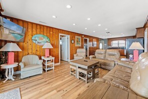 A spacious living room with wooden paneling, a poolside view, and a kitchen area. - Sea Aire II Duplex Up, Pet Friendly, Oceanfront, Shared Game Room (North Myrtle Beach)