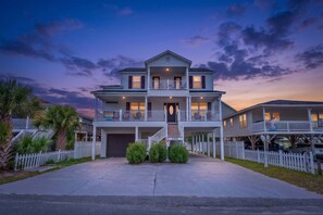 A two-story residential building with a front porch, a garage, and a balcony on the second floor. - Uptown Girl - 4 Bed/4 Bath House a Block from the Beach with Oceanview Balcony, Walk to Pier (North Myrtle Beach)