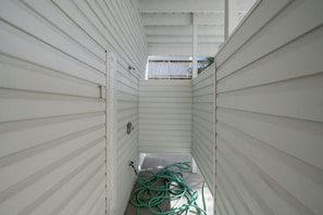 A narrow hallway with white siding walls and a visible window at the end.