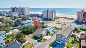 Un quartier résidentiel situé sur la côte, composé d’un mélange de maisons à un ou plusieurs étages, avec une plage en arrière-plan et une grande flèche rouge bien visible qui indique une maison en particulier.