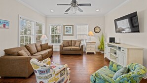 Un salon avec un ventilateur de plafond, deux canapés, une table basse, un téléviseur et un meuble.