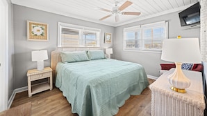 A bedroom with a bed, two bedside tables, a ceiling fan, and a TV on the wall.