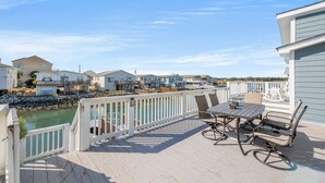 A wooden deck with a table and chairs, overlooking a body of water and a row of houses.