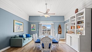 A dining area with a table and chairs, a ceiling fan, and a view of the outside.