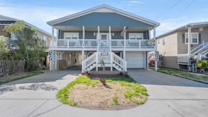 A two-story residential building with a front porch, a small garden, and a garage.