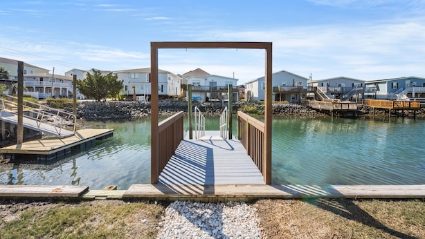 A wooden pier leading to a dock with a clear view of houses in the background.