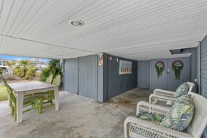 A covered patio area with a table and chairs, a grey wall with decorative wreaths, and a view of the outside.
