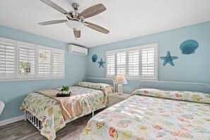 A bedroom with two beds, a ceiling fan, and decorative seashells on the wall.