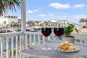 A balcony with two glasses of red wine and a plate of cheese, overlooking a marina with boats and buildings.