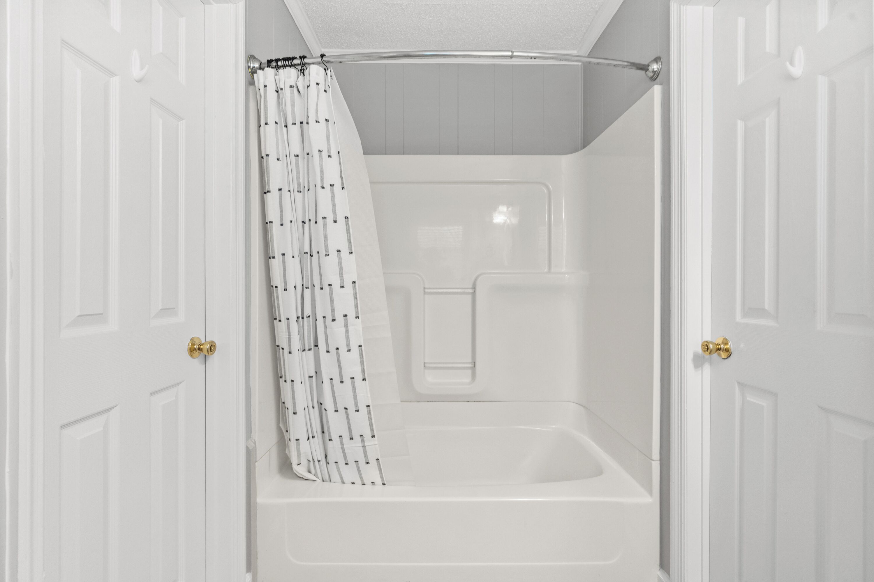 Une salle de bain blanche avec une baignoire, un rideau de douche et une porte dotée d’une poignée en laiton.
