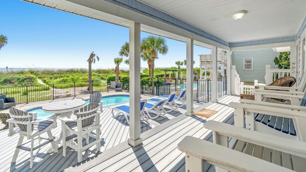 Um deck coberto ao ar livre com piscina, cadeiras de descanso e vista para o oceano.