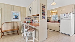 A kitchen with wooden cabinets, a white refrigerator, and a wooden bench with chairs.