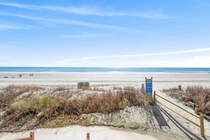 A beach with a wooden boardwalk, sandy dunes, and a clear blue sky.