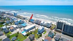 A coastal hotel with a pool, beachfront view, and a pier in the background.