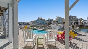 A pool area with white and yellow chairs, a small table, and a view of the surrounding buildings. - Sea La Vie, Luxury Channel Home in Cherry Grove, Beautiful Waterfront Pool Area (North Myrtle Beach)