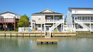 A waterfront property with a dock, a two-story house with a balcony, and a separate building with a staircase. - Sea La Vie, Luxury Channel Home in Cherry Grove, Beautiful Waterfront Pool Area (North Myrtle Beach)
