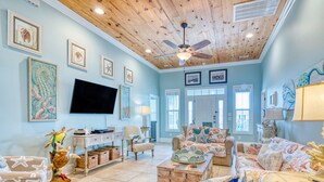 A spacious living room with a wooden ceiling, a flat-screen TV, and various framed artworks. - Sea La Vie, Luxury Channel Home in Cherry Grove, Beautiful Waterfront Pool Area (North Myrtle Beach)