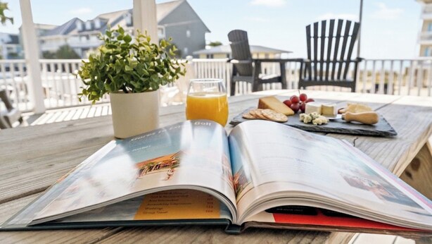 An open magazine on a wooden table with a potted plant, a glass of orange juice, cheese, and crackers. - Summer Fun - Beach Across the Street (North Myrtle Beach)