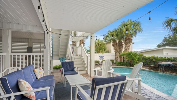 Un espacio al aire libre cubierto con una piscina, mobiliario blanco y una escalera que lleva a una terraza cubierta.