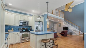 Cocina amplia con armarios blancos, encimera azul y una isla central con taburetes.