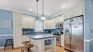Una cocina con armarios blancos, encimera azul, refrigerador de acero inoxidable y un taburete de bar.