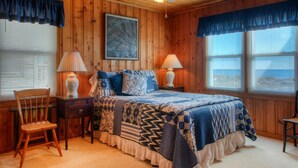 A wooden cabin bedroom with a bed, two lamps, a chair, and a ceiling fan. - Summer Rates Reduced at Magnificent Surf (North Myrtle Beach)