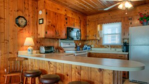 A wooden cabin-style kitchen with a central island, bar stools, a microwave, stove, and a refrigerator. - Summer Rates Reduced at Magnificent Surf (North Myrtle Beach)