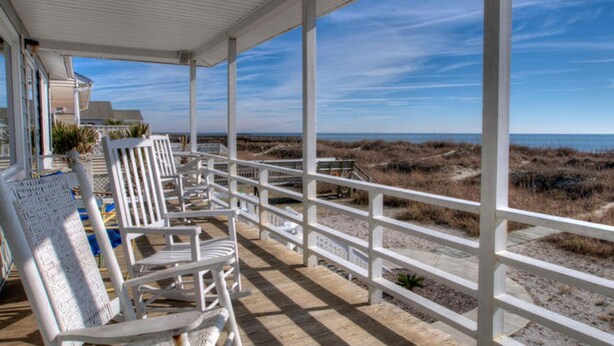 A covered outdoor area with white railings, white chairs, and a view of the beach. - Summer Rates Reduced at Magnificent Surf (North Myrtle Beach)