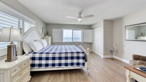 A bedroom with a bed, a ceiling fan, a nightstand, a dresser, a window with blinds, and a door.