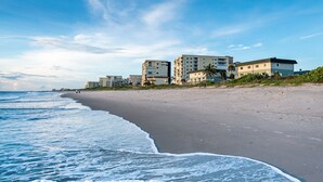 A beach with a row of multi-story buildings, some with balconies, and a clear sky.
