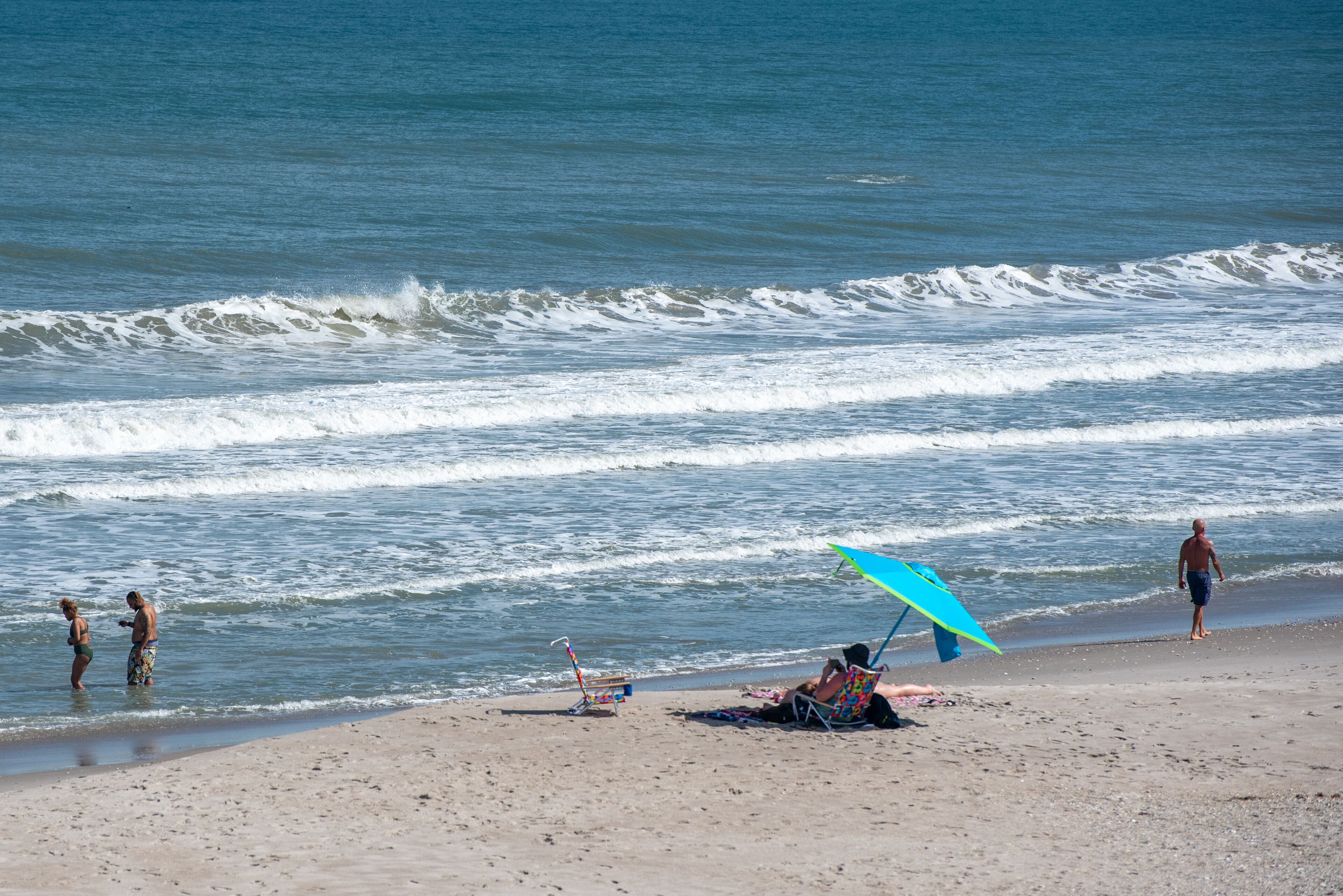Ein Strand mit Menschen, einem Stuhl und einem Sonnenschirm.