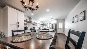 Una cocina moderna con armarios blancos, una isla central y un comedor con mesa y sillas de madera.