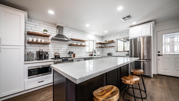 Una cocina moderna con armarios blancos, una isla grande y taburetes de bar.