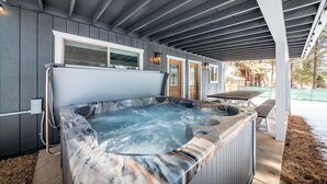 Un jacuzzi bajo un porche cubierto con revestimiento de madera, una puerta y vistas a un jardín trasero.