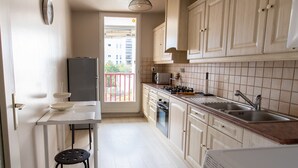 A compact kitchen with a refrigerator, stove, sink, and a small dining table with a stool. - T3 3* apartment in the heart of Anglet, a few minutes from the beaches (Anglet)