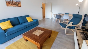 A living room with a blue sofa, a wooden coffee table, and a dining area with a table and chairs. - T3 3* apartment in the heart of Anglet, a few minutes from the beaches (Anglet)