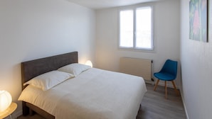 A bedroom with a bed, a chair, a radiator, and a window. - T3 3* apartment in the heart of Anglet, a few minutes from the beaches (Anglet)