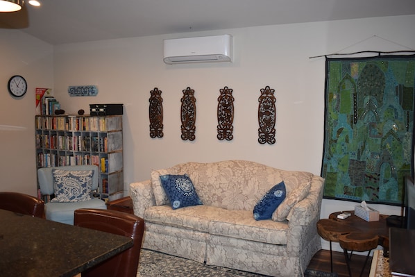 Un salón acogedor con un sofá estampado, una estantería, detalles decorativos en la pared y un ventanal grande.
