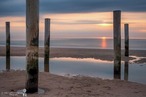 A beach scene with wooden posts and calm water reflecting the sunset.