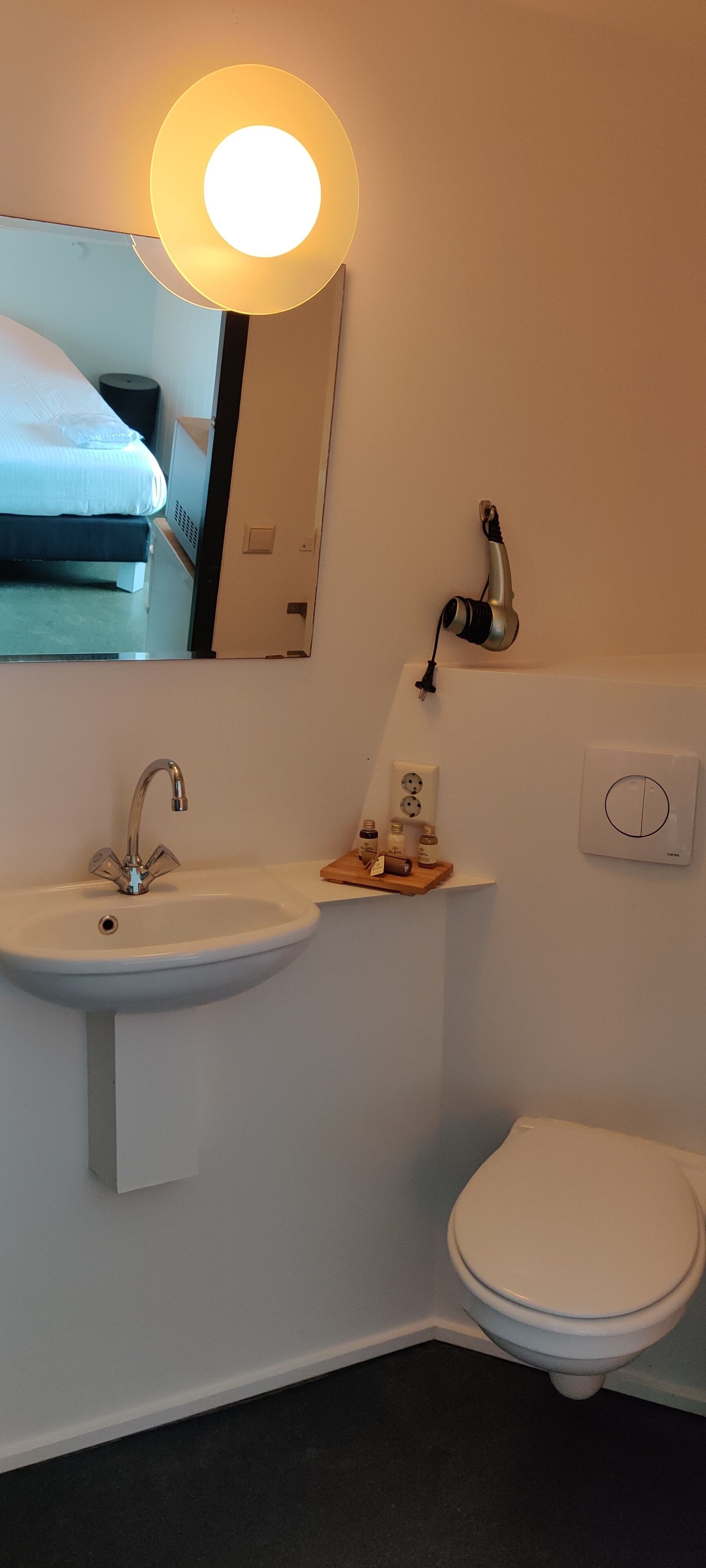 Ein Badezimmer mit einem weißen Waschbecken, einem Spiegel, einer Toilette und einem Haartrockner auf einem Regal.