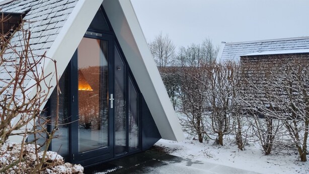 Una casa moderna con un tetto triangolare e un'ampia porta vetrata che dà su un interno illuminato.