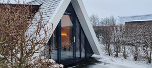 Ein modernes Haus mit einem dreieckigen Dach und einer Glastür, die zu einem beleuchteten Innenraum führt.