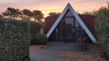 Un bâtiment moderne avec un toit triangulaire et une porte en verre, entouré de haies et avec un vélo garé devant.