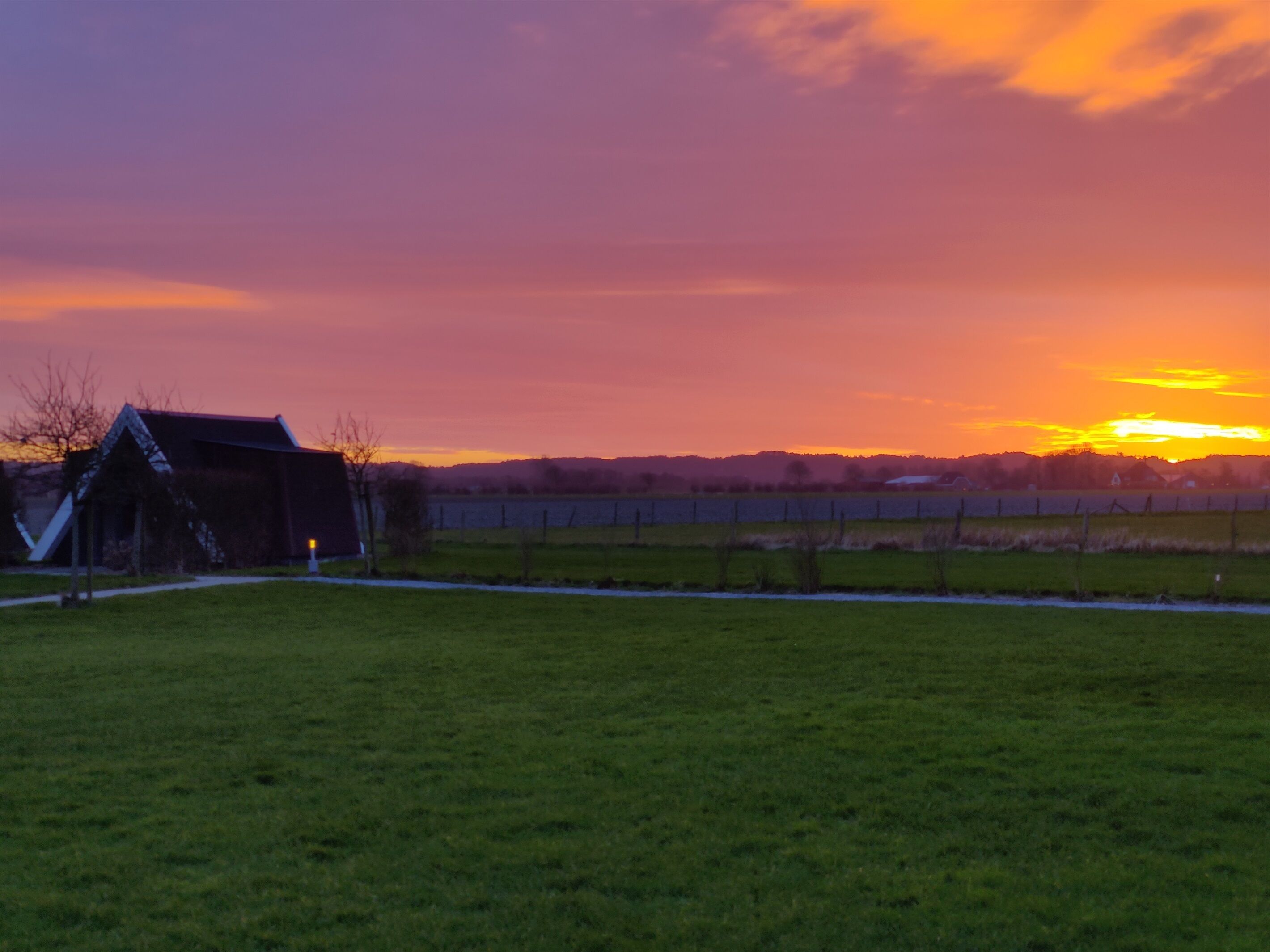 A rural landscape with a barn and open fields during sunset.